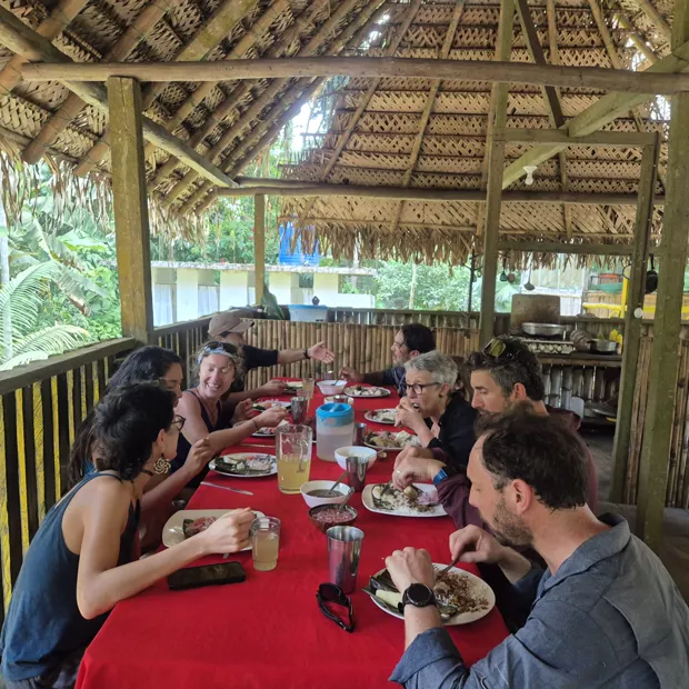 Everyone eating together at the long red table under the thatch