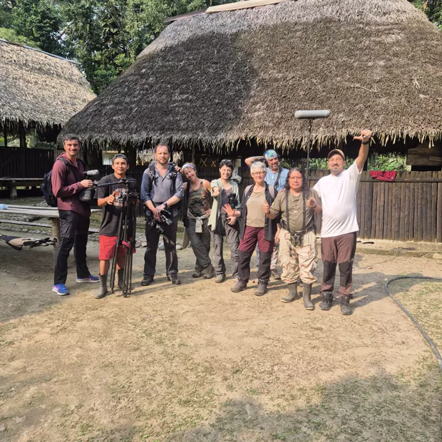 Waorani community members posing in front of a thatched building