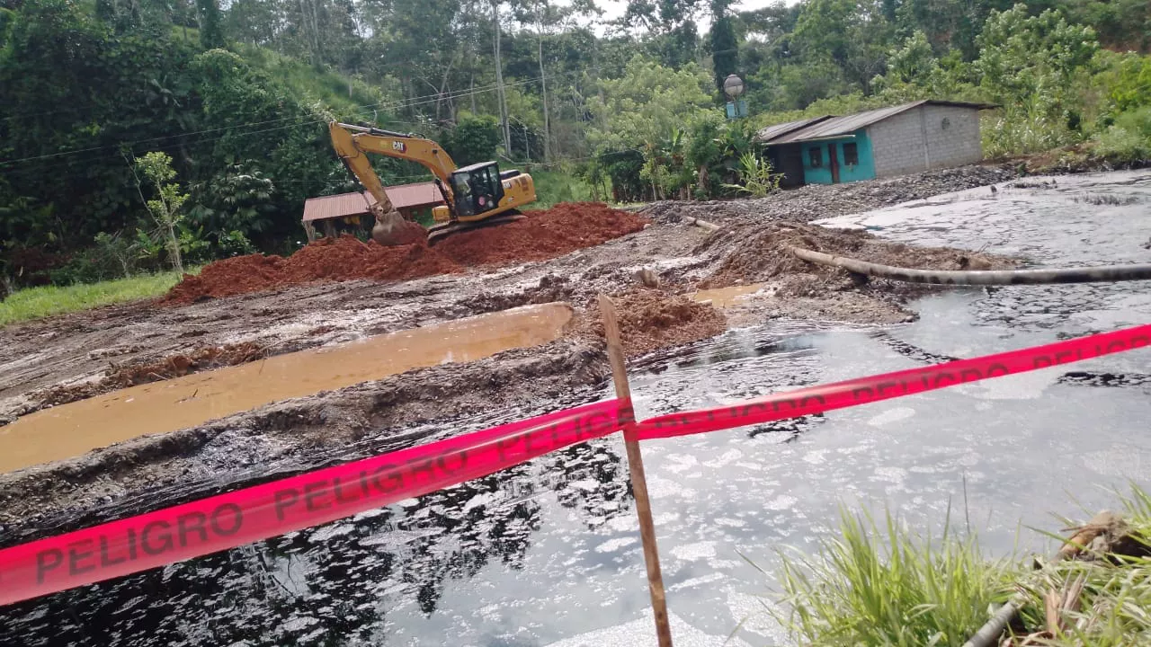 Oil waste pit with hazard tape and an excavator moving earth next to a house